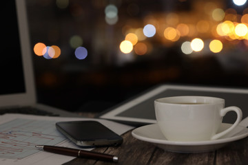 overtime in the evening, work from home, a cup of coffee and a laptop on a night background with beautiful bokeh