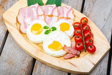 Tasty fried eggs with vegetables on a wooden plate.
