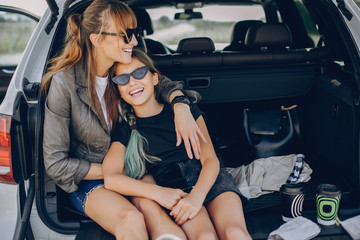Fashionable mother with daughter. Family is sitting in the trunk. Girl in a black t-shirt