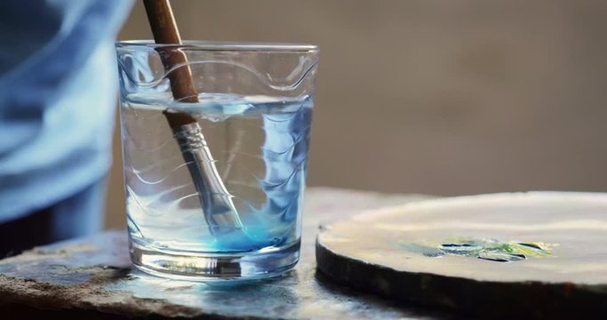 Elderly people painting for hobby. Active senior person at school of arts. Leisure activity, lifestyle, recreation, passion, fun. Closeup of old brush being cleaned in glass of water. Slow motion
