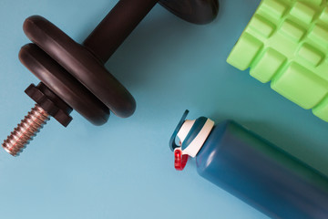 Sport dumbell whith metallic bottle of water and foam roller on blue background. Fitness background. Healthy lifestyle accessories.