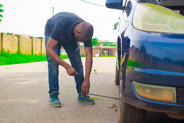 Young African man wearing a hard hat sitting while trying to  change his tyre