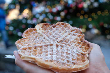 Selective focus two hands holding one tasty waffle with icing (powdered )sugar. Blurred colourful...