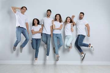Group of young people in stylish jeans jumping near light wall