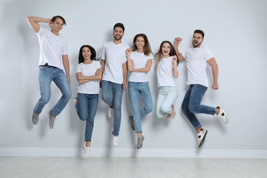 Group Of Young People In Stylish Jeans Jumping Near Light Wall