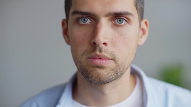 Head and shoulders closeup video portrait of serious Caucasian young man with stubble on his face looking at camera