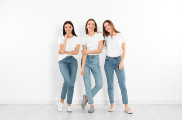 Group of young women in stylish jeans near white wall