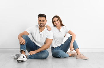 Fototapeta na wymiar Young couple in stylish jeans sitting near white wall