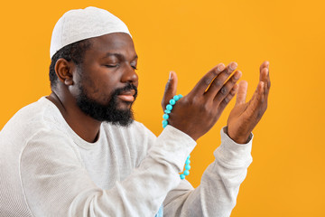 African-American Muslim man praying against color background