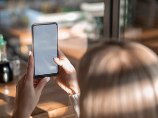 Mockup blonde woman watching her smartphone with empty screen in a cafe