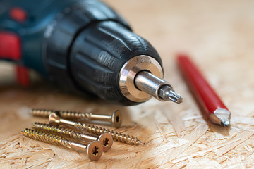 Electric screwdriver, self drilling screws and carpenter pencil lying on chip board. Blurred...