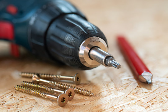 Electric screwdriver, self drilling screws and carpenter pencil lying on chip board. Blurred background.