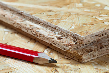 Red carpenter pencil lying next to tongue and groove chip board. Blurred background.