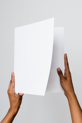 Black, Southeast Asian or ethnic model holding a blank mock-up or dummy of an A5 or half letter-sized brochure or report with both hands. Studio shot on white.