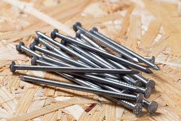 A pile of steel nails lying on chip board. Blurred background.