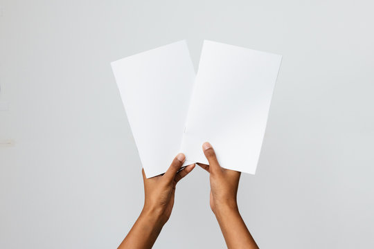 Black, Southeast Asian or ethnic model holding two blank mock-ups or dummies of A4 or letter sized brochures or reports. Studio shot on white. Ideal to place art of two publications for comparison.