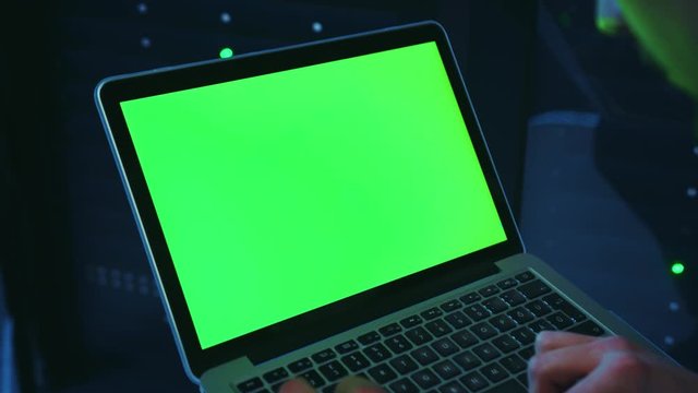 IT administrator using a mock-up notebook running neural network to control secure server cabinet, looking at green template monitor working at data center. Cyber security,