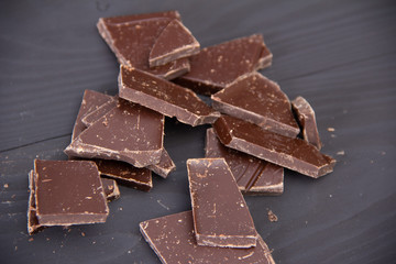 Broken dark chocolate on wooden background.