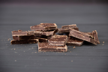 Broken dark chocolate on wooden background.
