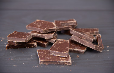 Broken dark chocolate on wooden background.