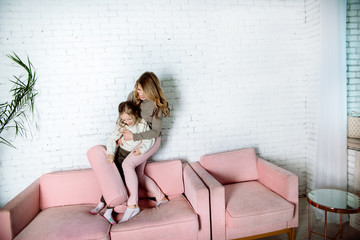 Parental love, upbringing and care.Happy mommy and kid daughter holding hands jumping on sofa together, baby sitter or mother playing having fun with cute kid girl at home