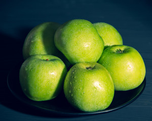 Green apples with water drops on black background.