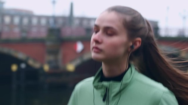 Portrait of beautiful sporty girl in earphones confidently running in autumn city park
