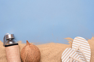 Sea vacation background with copy space. Coconut, flip flops and cocktail bottle on the sand over...