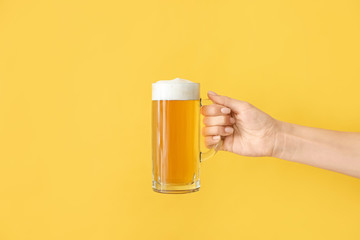 Hand with mug of beer on color background