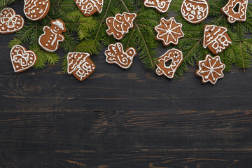 Christmas composition of homemade gingerbread and spruce branches on a black wooden background.