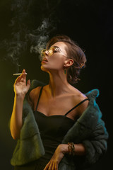 Obraz premium A young beautiful girl in glasses and a fur coat smokes a cigarette.