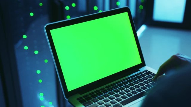 IT technician running diagnostics on mock-up greenscreen laptop deactivating a server cabinet database. Close-up specialist recoding program on notebook operating data center server.