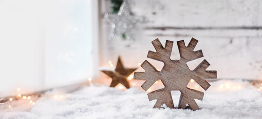 Scandinavian styled christmas background - a big wooden snowflake on a bright white snowy scene beside a window - 308830092