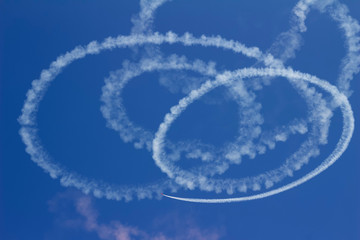 Abstract view of the vapor trail of an airplane skywriting in spiraling circles against a deep blue sky