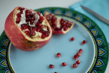 Large ripe pomegranate and scattered grains on a turquoise plate with a metal knife on a plaid napkin