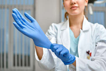 Close up of a female doctor putting a blue latex gloves on a clinic background.