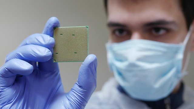 Young engineer in mask holds in hand CPU processor. Quality control laboratory for manufacturing technological computer devices