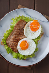  Fried egg and steak on bread for breakfast on plate and rustic table