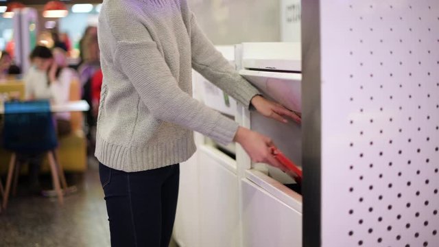 girl throws trash from a tray on a supermarket food court into a special container