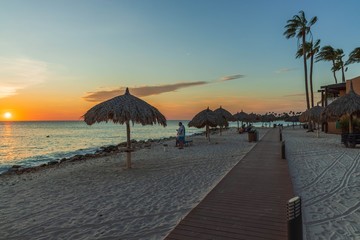 Beautiful view of coast line hotel area on sunset. White sand beach. sun umbrellas and palm trees on blue sky background. Tamarijn hotel.Oranjestad. Aruba.