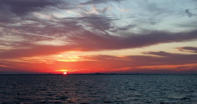 A colorful sunrise paints a cloudy sky with color over San Carlos Bay with Fort Myers Beach, Florida on the horizon in this seamless motion background video loop