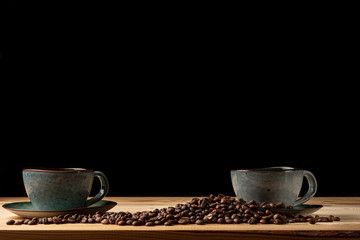 Handmade cup with coffee on the table. Countertop made of wood. Coffee beans. Black background.
