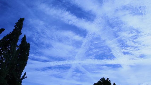 Panning across a geoengineered sky of homomutatus clouds that have been created by spraying chemtrails. The shape of the letter A can be seen with the crisscross of the aluminum trails. They spread.