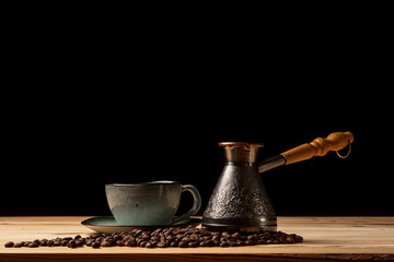 Copper cezve with coffee on the table. Freshly brewed coffee. Countertop made of wood. Coffee beans. Freshly fried arabica. Black background.