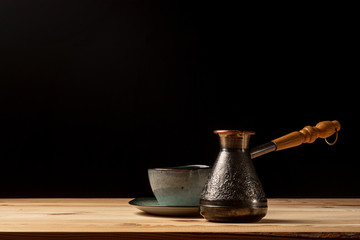 Copper cezve with coffee on the table. Freshly brewed coffee. Countertop made of wood. Coffee beans. Freshly fried arabica. Black background.