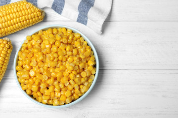 Delicious canned corn in bowl on white wooden table, flat lay. Space for text