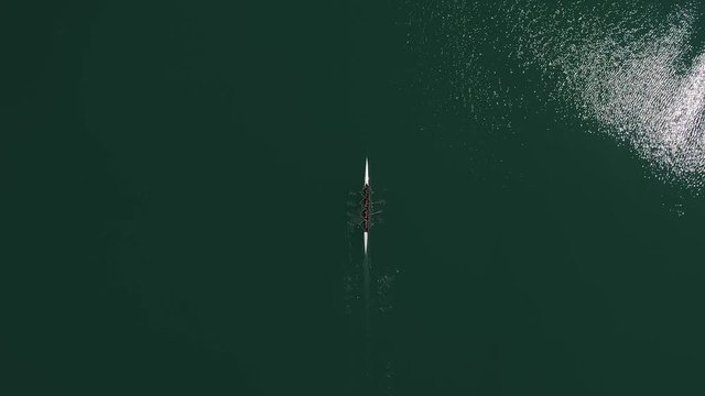 Overhead aerial view of rowing team in boat rowing together in green open water.