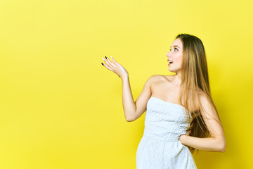 Portrait of a cheerful young lady smiling presenting your product. Woman points to copyspace. Isolated on a yellow background.