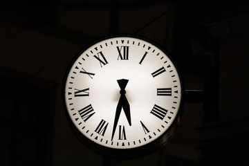 white old antique luminous clock with hour and minute hands in front of black background