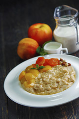Oatmeal porridge with apples and cinnamon on a black wooden table.